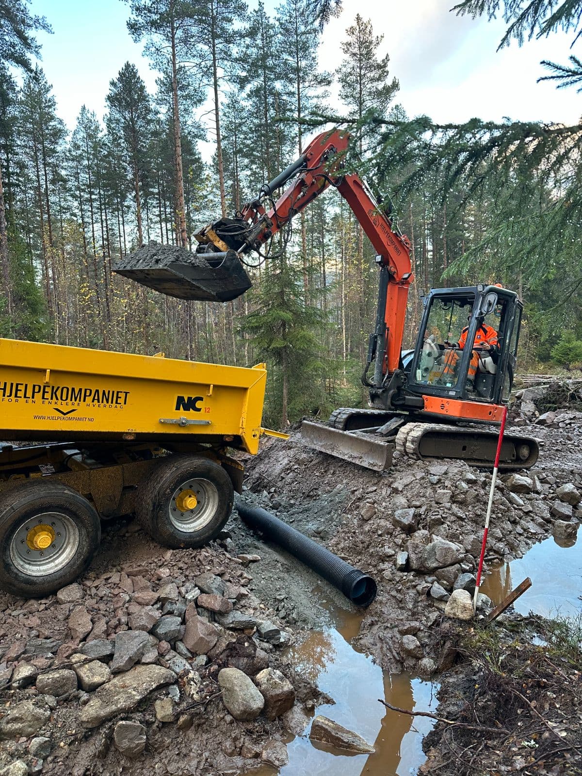 Gravemaskin legger drensrør, med tipphenger fra Hjelpekompaniet ved siden av